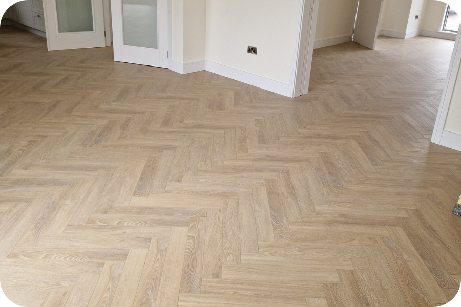 Empty room with light-colored wood flooring arranged in a herringbone pattern, white walls, white baseboards, and several doorways leading to other rooms.